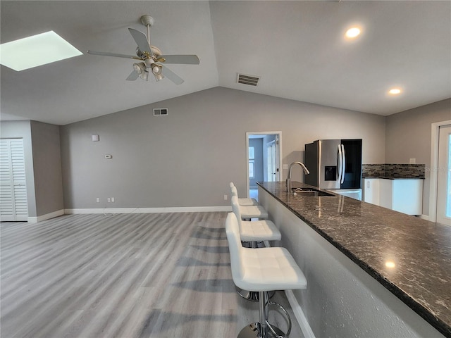 kitchen featuring vaulted ceiling, dark stone counters, sink, stainless steel fridge, and light wood-type flooring