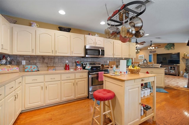 kitchen featuring ceiling fan, appliances with stainless steel finishes, tasteful backsplash, light wood-type flooring, and lofted ceiling