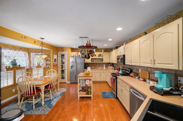 kitchen featuring white cabinetry, light hardwood / wood-style floors, appliances with stainless steel finishes, decorative backsplash, and hanging light fixtures