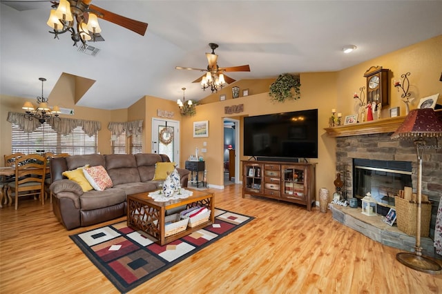 living room with lofted ceiling, ceiling fan with notable chandelier, light hardwood / wood-style flooring, and a stone fireplace