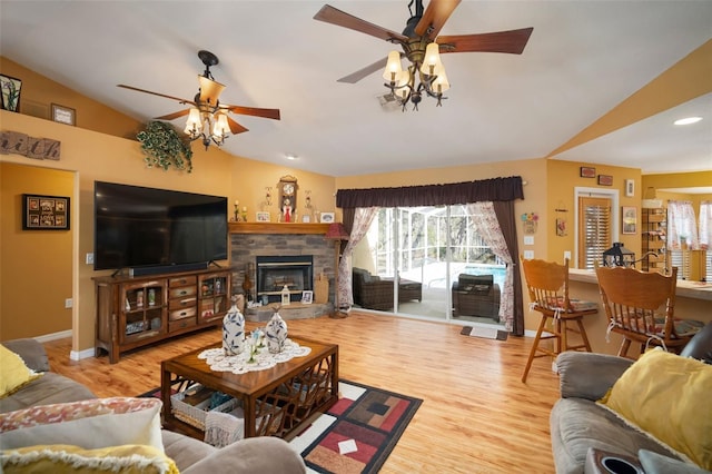 living room featuring ceiling fan, vaulted ceiling, a stone fireplace, and light hardwood / wood-style flooring