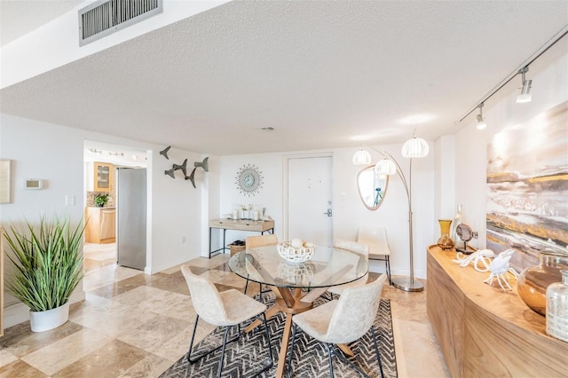 dining space with rail lighting and a textured ceiling