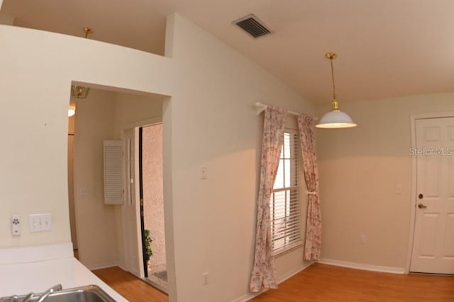 unfurnished dining area with baseboards, visible vents, lofted ceiling, wood finished floors, and a sink