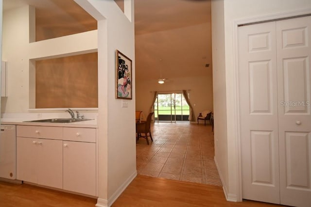 corridor with baseboards, a sink, and light wood-style floors