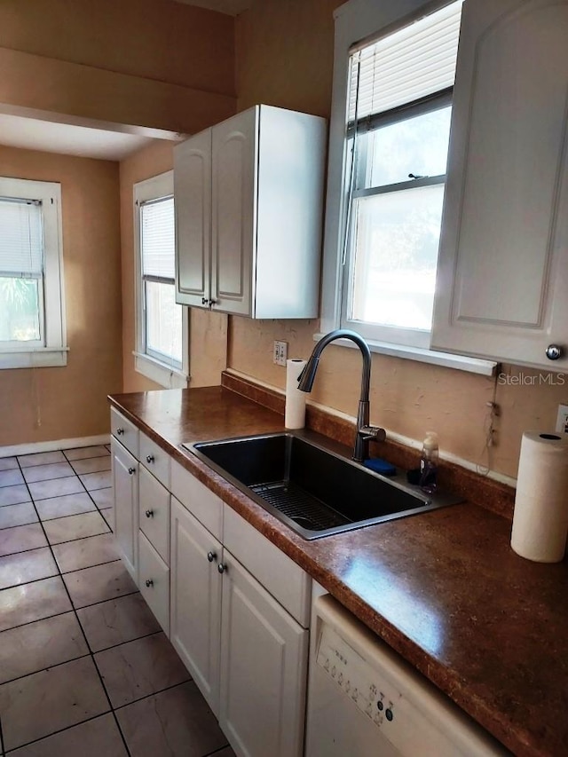 kitchen with sink, light tile patterned floors, dishwasher, and white cabinets