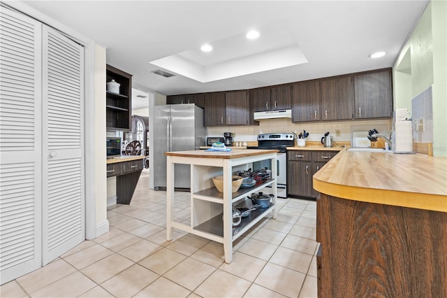 kitchen featuring kitchen peninsula, appliances with stainless steel finishes, a tray ceiling, light tile patterned flooring, and dark brown cabinetry