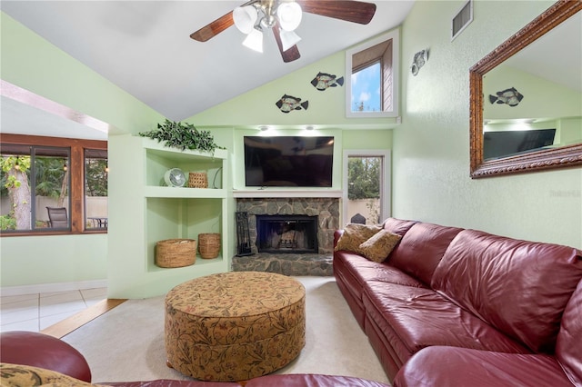 tiled living room featuring vaulted ceiling, ceiling fan, a stone fireplace, and built in shelves