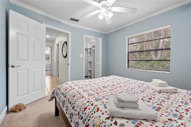 bedroom with light carpet, ceiling fan, a closet, ornamental molding, and a walk in closet