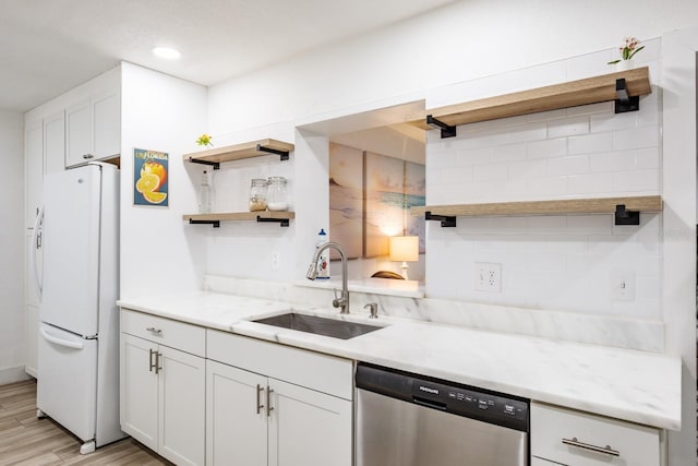 kitchen featuring stainless steel dishwasher, sink, white refrigerator, white cabinets, and light stone countertops