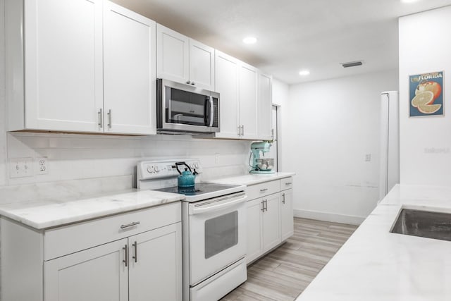 kitchen featuring backsplash, white cabinets, light wood-type flooring, light stone countertops, and electric range