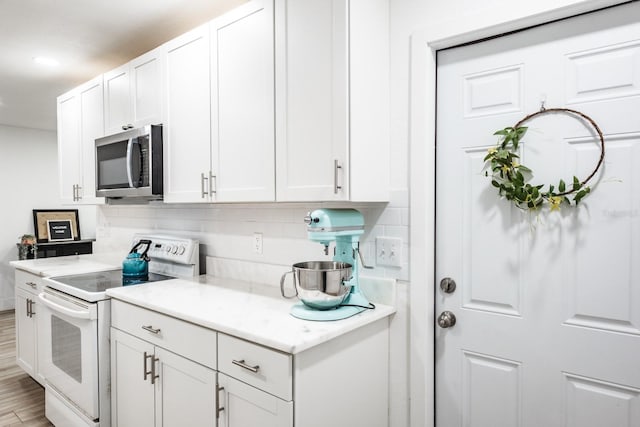 kitchen featuring white range with electric cooktop, white cabinets, light stone counters, light hardwood / wood-style floors, and decorative backsplash