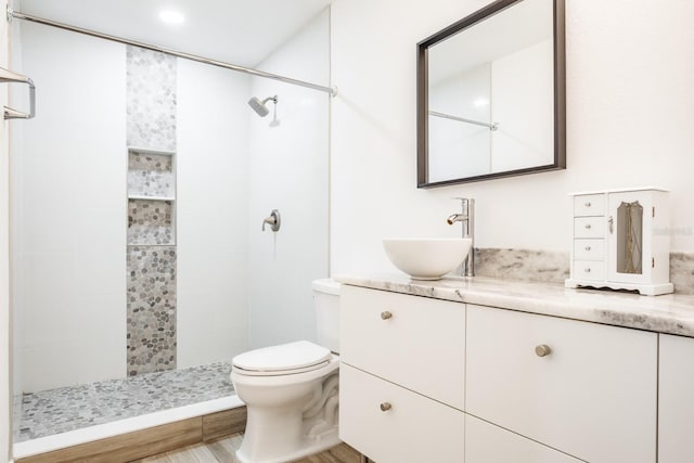 bathroom featuring a tile shower, hardwood / wood-style flooring, toilet, and vanity