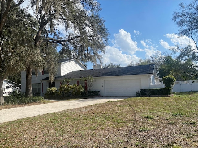 traditional-style home featuring concrete driveway, a front lawn, an attached garage, and fence