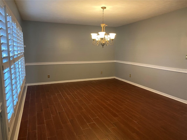 unfurnished room featuring dark wood-type flooring, a chandelier, and baseboards