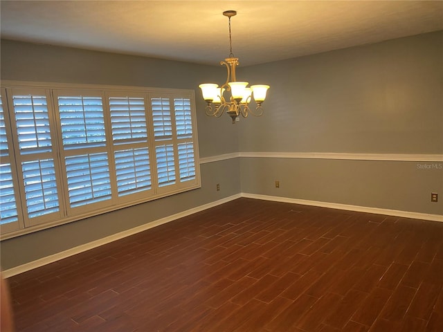 spare room with dark wood finished floors, a notable chandelier, and baseboards