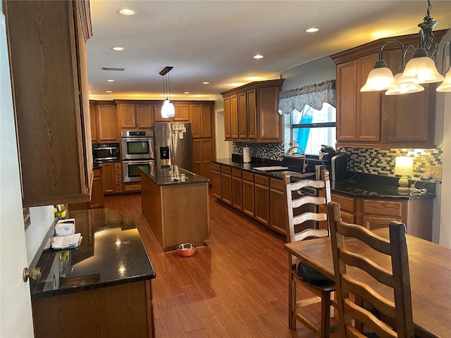 kitchen featuring stainless steel appliances, dark stone counters, tasteful backsplash, dark wood finished floors, and a center island with sink