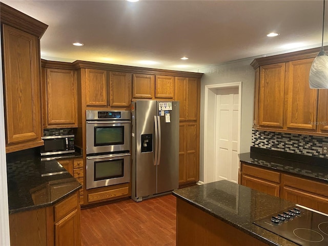 kitchen featuring brown cabinetry, decorative backsplash, dark stone counters, appliances with stainless steel finishes, and dark wood-style flooring