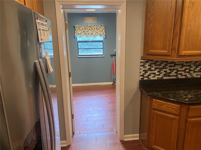 kitchen with brown cabinetry, dark stone counters, wood finished floors, stainless steel refrigerator with ice dispenser, and backsplash