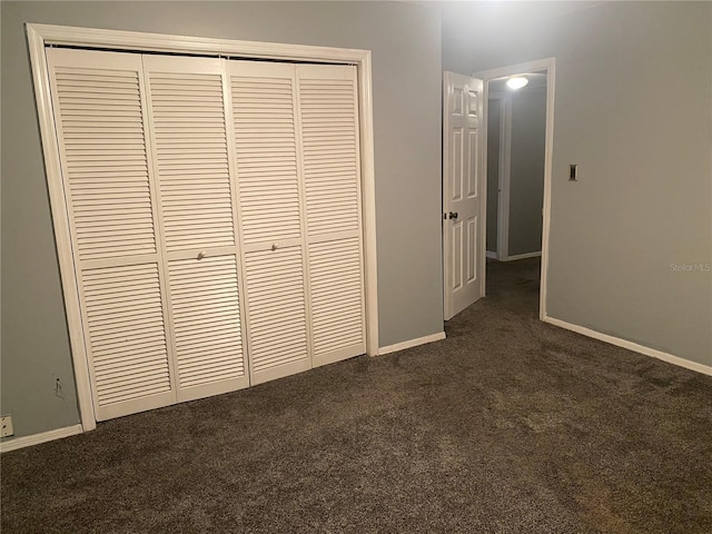 unfurnished bedroom with baseboards, dark colored carpet, and a closet