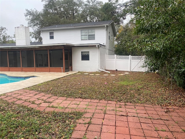 rear view of house featuring a fenced in pool, a chimney, a sunroom, a gate, and fence