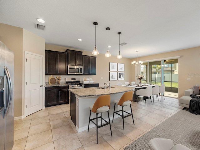 kitchen featuring hanging light fixtures, light tile patterned floors, stainless steel appliances, a center island with sink, and a breakfast bar area