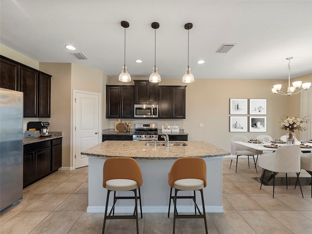 kitchen with a kitchen island with sink, sink, dark brown cabinetry, pendant lighting, and stainless steel appliances