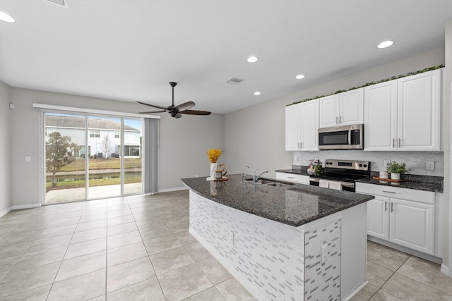 kitchen featuring appliances with stainless steel finishes, white cabinetry, dark stone countertops, an island with sink, and sink