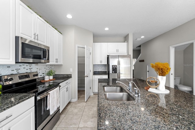 kitchen featuring appliances with stainless steel finishes, white cabinetry, light tile patterned floors, sink, and dark stone counters