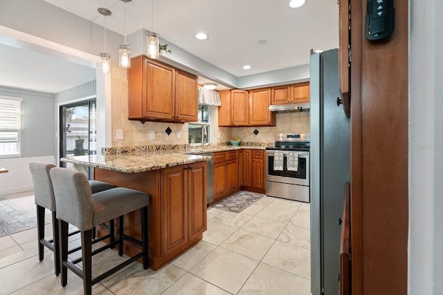 kitchen with a kitchen bar, stainless steel appliances, hanging light fixtures, kitchen peninsula, and light stone counters