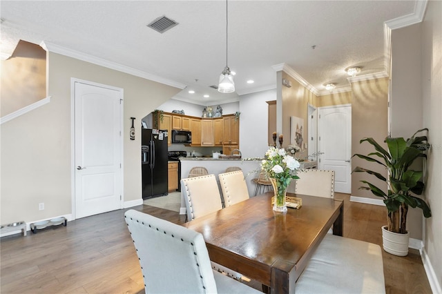 dining space with a textured ceiling, ornamental molding, and light wood-type flooring