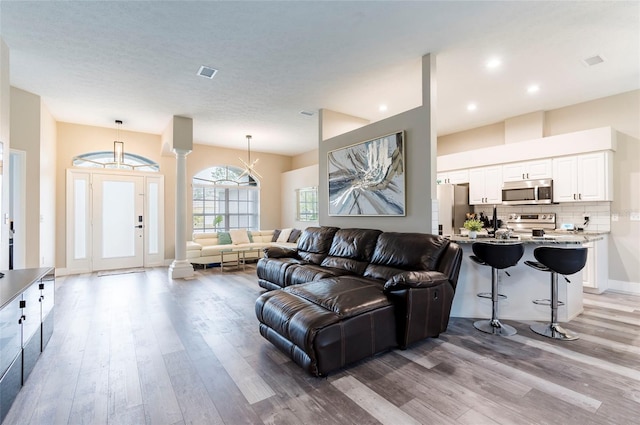 living room featuring ornate columns, a notable chandelier, and light hardwood / wood-style flooring