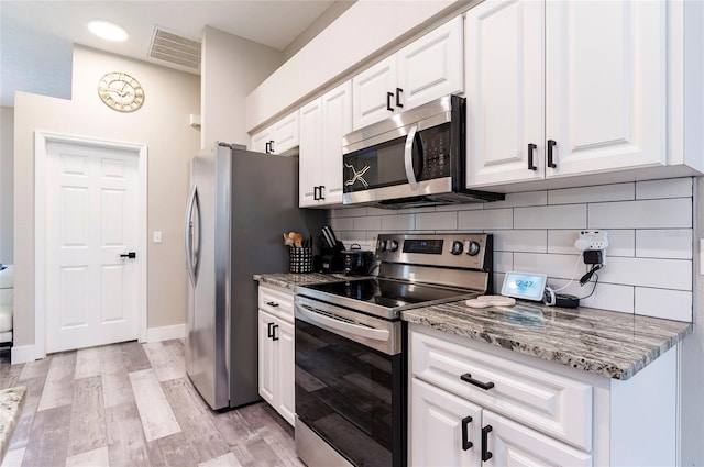 kitchen with appliances with stainless steel finishes, white cabinets, backsplash, light stone counters, and light wood-type flooring