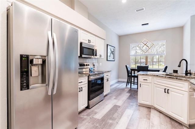 kitchen with sink, white cabinetry, decorative light fixtures, stainless steel appliances, and light stone countertops