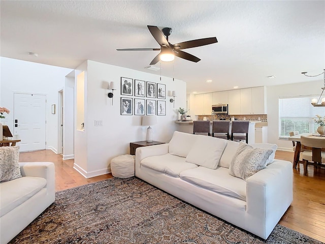 living room with ceiling fan with notable chandelier, light hardwood / wood-style floors, and a textured ceiling