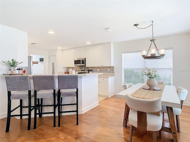 kitchen featuring white cabinetry, an inviting chandelier, decorative light fixtures, light wood-type flooring, and backsplash