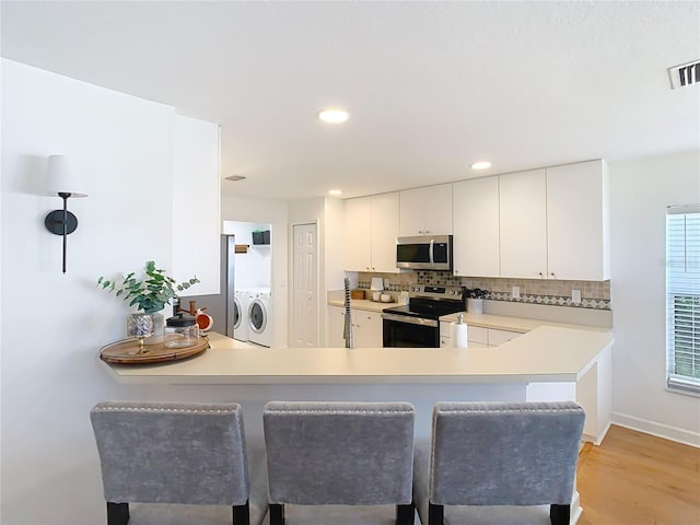 kitchen featuring white cabinetry, stainless steel appliances, washer and dryer, and kitchen peninsula