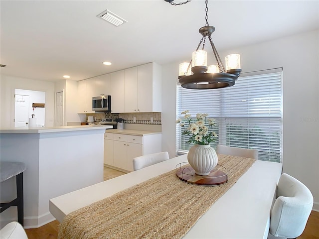 kitchen featuring appliances with stainless steel finishes, decorative light fixtures, white cabinetry, backsplash, and a notable chandelier