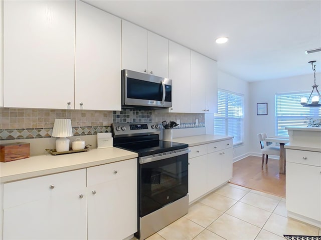 kitchen with appliances with stainless steel finishes, pendant lighting, tasteful backsplash, white cabinets, and light tile patterned floors