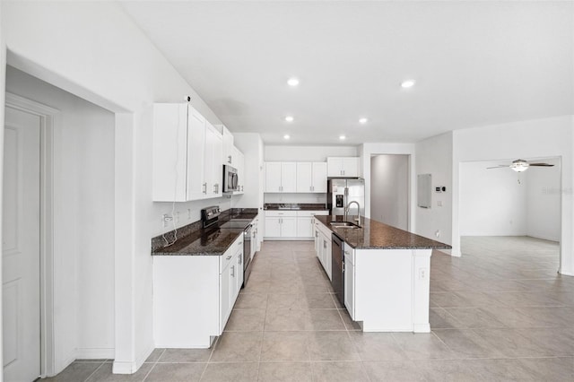 kitchen with white cabinets, appliances with stainless steel finishes, dark stone countertops, sink, and a center island with sink