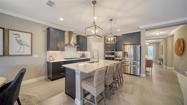 kitchen featuring appliances with stainless steel finishes, wall chimney range hood, sink, a breakfast bar, and a center island with sink