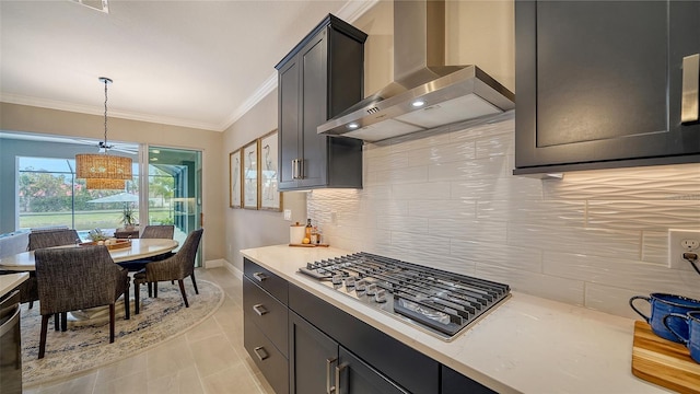 kitchen with light tile patterned floors, crown molding, appliances with stainless steel finishes, hanging light fixtures, and wall chimney exhaust hood