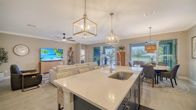 kitchen with ornamental molding, an island with sink, hanging light fixtures, and sink