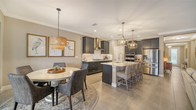 kitchen featuring a breakfast bar area, appliances with stainless steel finishes, wall chimney exhaust hood, a kitchen island with sink, and pendant lighting