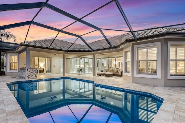 pool at dusk featuring glass enclosure, a patio area, outdoor lounge area, and ceiling fan