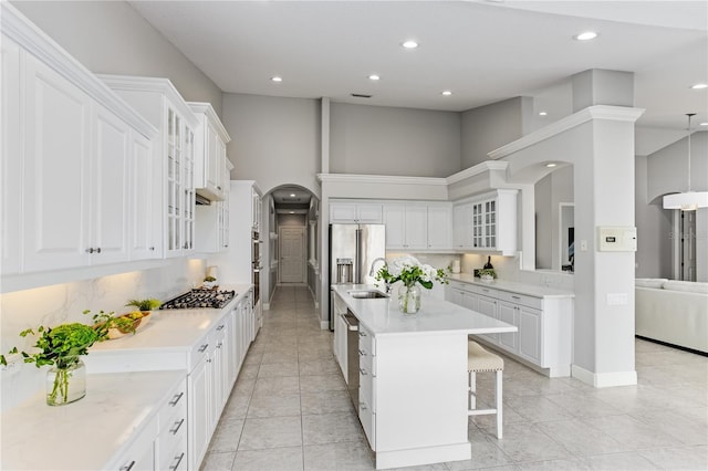 kitchen with white cabinets, a towering ceiling, a kitchen island, sink, and a breakfast bar area