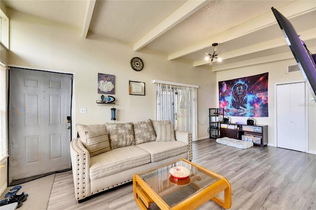 living room with a textured ceiling, beamed ceiling, and light wood-type flooring