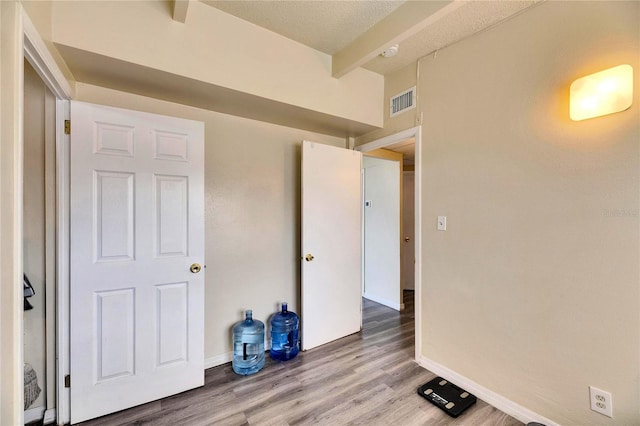 spare room featuring a textured ceiling, hardwood / wood-style flooring, and beamed ceiling