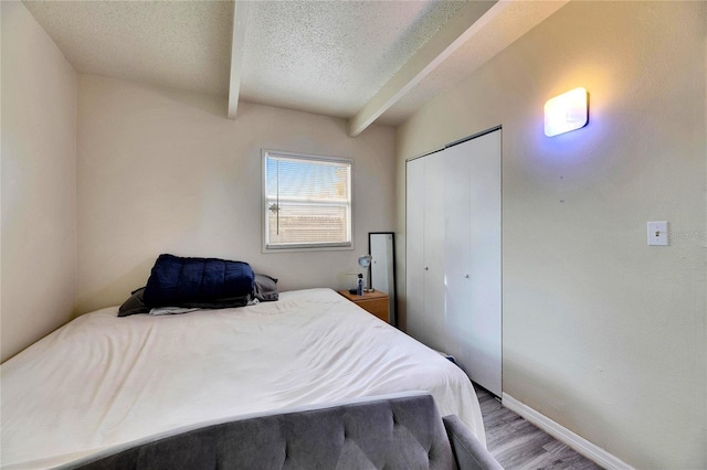 bedroom with beam ceiling, a closet, a textured ceiling, and light hardwood / wood-style flooring