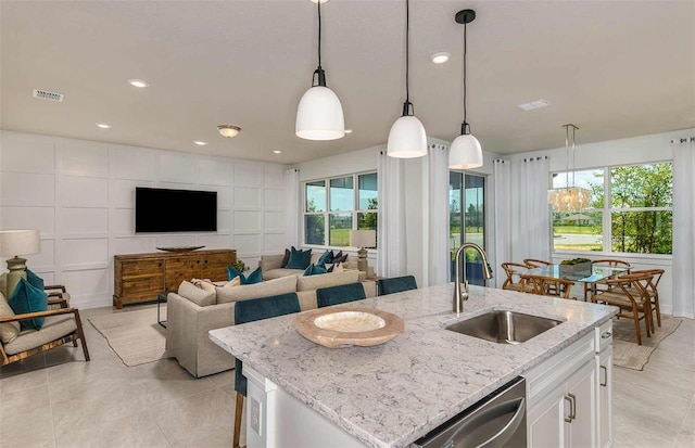 kitchen with white cabinets, decorative light fixtures, an island with sink, sink, and light stone counters