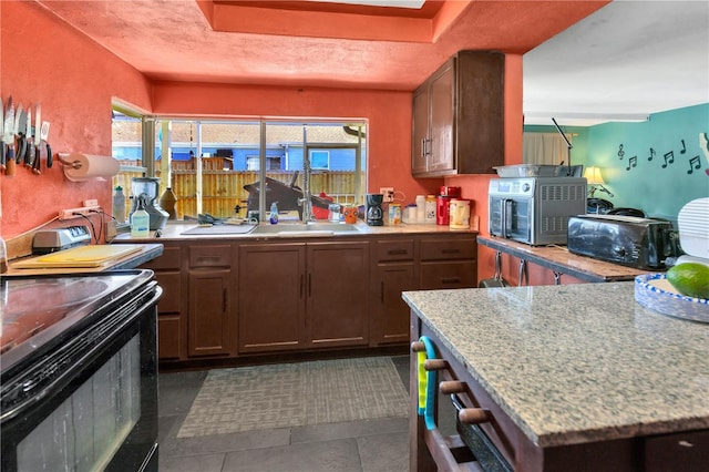 kitchen with light stone countertops, dark tile patterned floors, black range with electric stovetop, and sink